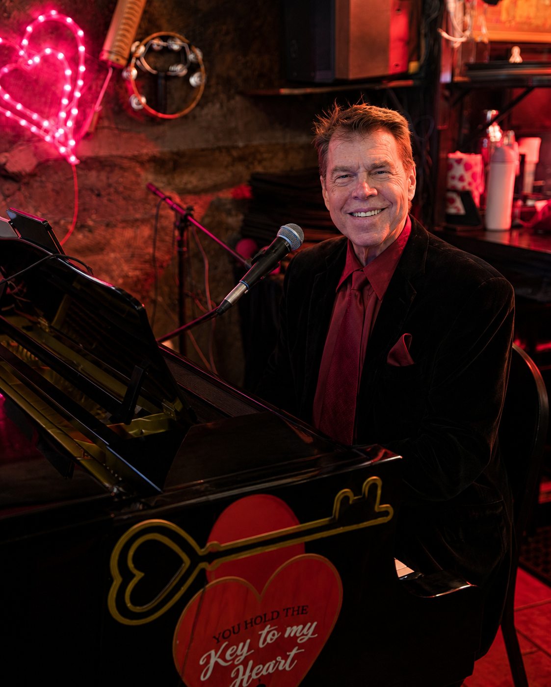 Michael Kevin Walsh at the piano at Da Marino in New York City, a neon heart glowing behind him